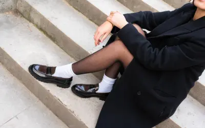 Schwarzer Mantel, schwarze Strumpfhose und weiße Socken mit glänzenden braunen Loafern.