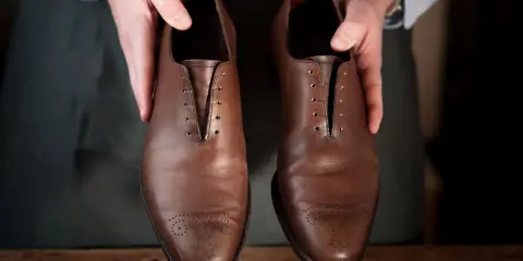 Hände präsentieren braune Lederschuhe, bereit für die Fettleder Pflege.