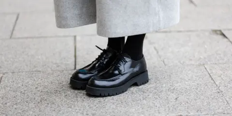 Schwarze Schnürschuhe mit dicker Sohle, ein moderner Schuh-Typ für Damen, kombiniert mit einem grauen Wollrock.