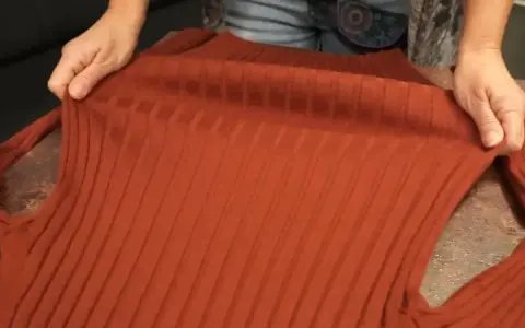 Hände halten einen verfilzten und eingelaufenen Pullover aus Rippstrick. Essig als Hausmittel zur Rettung?