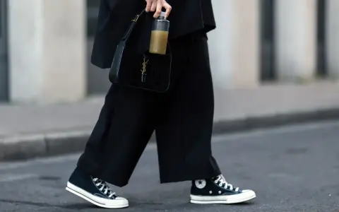 Schwarze, weite Hose und hohe Chucks kombinieren Damen für einen lässigen Look. Dazu eine schwarze Kroko-Tasche und eine Wasserflasche.