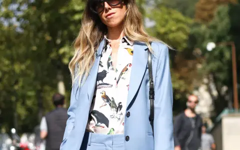 Eine Frau kombiniert einen blauen Blazer mit einem Hemd mit Vogelmotiv und auffälliger Sonnenbrille.