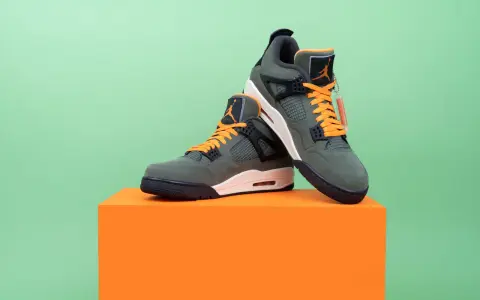 Jordan Motorsport Sneaker in Olivgrün mit orangefarbenen Schnürsenkeln, auf einem orangefarbenen Podest vor hellgrünem Hintergrund.