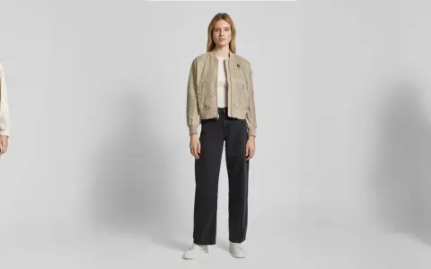 Drei Frauen präsentieren lässige Outfits. Die mittlere Frau zeigt, wie man eine Bomberjacke stylen kann, kombiniert mit weiten Jeans und Sneakern.