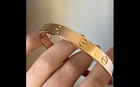 Vergleich: Fake Cartier Love Armband vs. echt. Ein glänzendes, roségoldenes Armband mit Schraubenmotiv wird von Fingern gehalten.