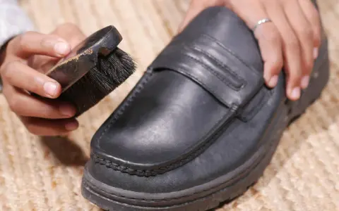 Hände reinigen einen schwarzen Lederschuh mit einer Bürste.