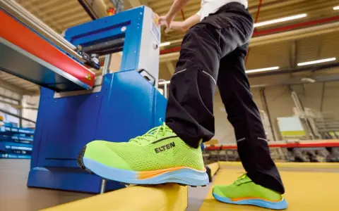 Arbeiter in leuchtend grünen Sicherheitsschuhen von ELTEN an einer Maschine. Seit wann gibt es Schuhe? Schon seit der Steinzeit, um die Füße zu schützen.