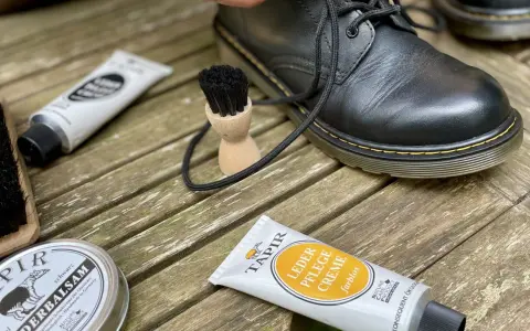 Schwarze Lederstiefel werden mit Tapir Lederpflegecreme und Bürsten gepflegt.