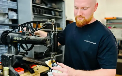 Ein Schuster repariert Schuhe an einer alten Nähmaschine. Er ist ein Handwerker, der sich um das Schuhwerk kümmert.