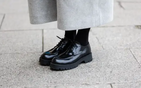 Schwarze Schnürschuhe mit dicker Sohle, ein moderner Schuh-Typ für Damen, kombiniert mit einem grauen Wollrock.