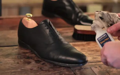 Schuhe polieren: Ein schwarzer Lederschuh mit Schuhspanner wird mit einem Tuch und Saphir Reno'Mat gereinigt.