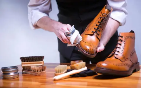 Mann poliert braune Glattleder-Schuhe mit einem Tuch. Pflege für Glattleder ist wichtig.