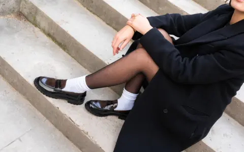 Schwarzer Mantel, schwarze Strumpfhose und weiße Socken mit glänzenden braunen Loafern.