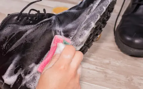Schwarze Lederschuhe werden mit einem Schwamm und Seifenschaum gereinigt. Die Sohle und das Leder werden sorgfältig abgerieben, um sie wieder sauber zu machen.