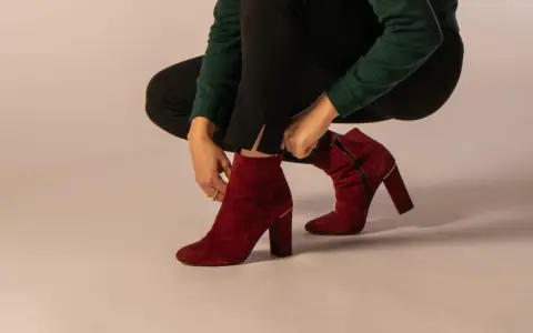Eine Frau zieht rote Wildleder-Stiefeletten an. Verschiedene lederarten schuhe sind hier zu sehen, wie diese eleganten Damenschuhe.