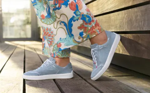Blaue Wildlederschuhe mit weißer Sohle und dezenter Ziernaht am Schuh, kombiniert mit einer Hose mit floralem Muster.