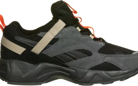 Reebok Aztrek 96: schwarzer Sneaker mit grauen Wildleder-Overlays, beige Akzenten und orangefarbenen Schlaufen.