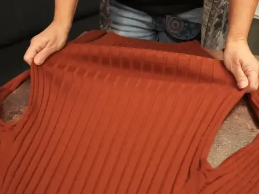 Hände halten einen verfilzten und eingelaufenen Pullover aus Rippstrick. Essig als Hausmittel zur Rettung?