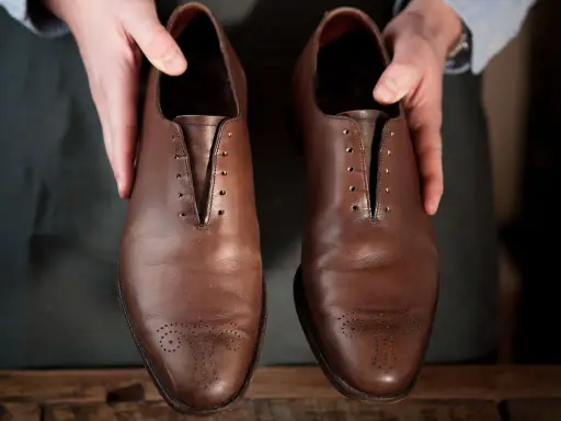 Hände präsentieren braune Lederschuhe, bereit für die Fettleder Pflege.