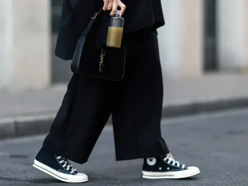 Schwarze, weite Hose und hohe Chucks kombinieren Damen für einen lässigen Look. Dazu eine schwarze Kroko-Tasche und eine Wasserflasche.