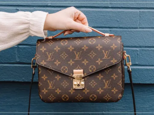 Eine Hand hält eine braune Louis Vuitton Tasche mit Monogramm-Muster. So erkennst du ein louis vuitton original.