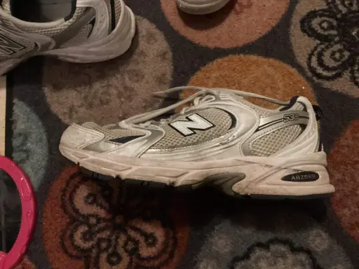 Ein schmutziger New Balance 530 Sneaker liegt auf einem gemusterten Teppich. Zeit, ihn zu waschen!