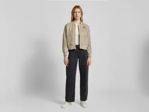 Drei Frauen präsentieren lässige Outfits. Die mittlere Frau zeigt, wie man eine Bomberjacke stylen kann, kombiniert mit weiten Jeans und Sneakern.
