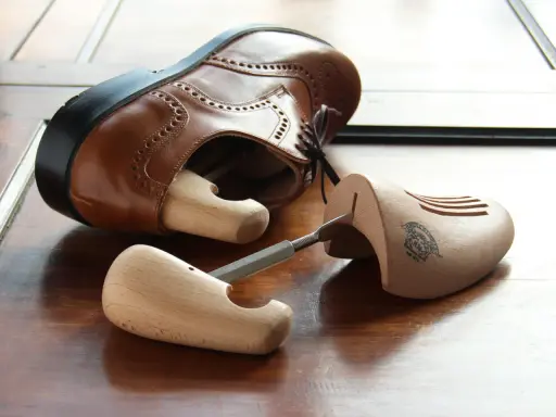 Holz-Schuhspanner für elegante Schuhe, die auch als Schuhspanner für Wanderschuhe dienen könnten, liegen neben einem braunen Lederschuh.