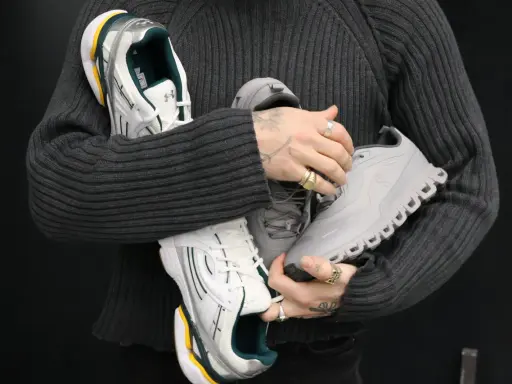Person hält drei Paar Sneaker: weiße mit grünen Akzenten, graue und silberne. Ein Blick auf modernes shoe design.