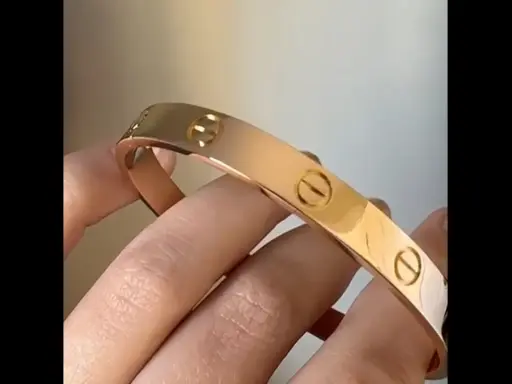 Vergleich: Fake Cartier Love Armband vs. echt. Ein glänzendes, roségoldenes Armband mit Schraubenmotiv wird von Fingern gehalten.