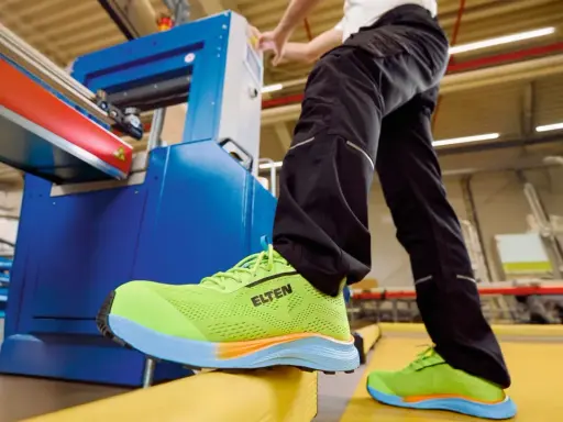 Arbeiter in leuchtend grünen Sicherheitsschuhen von ELTEN an einer Maschine. Seit wann gibt es Schuhe? Schon seit der Steinzeit, um die Füße zu schützen.