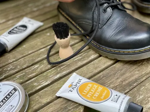 Schwarze Lederstiefel werden mit Tapir Lederpflegecreme und Bürsten gepflegt.
