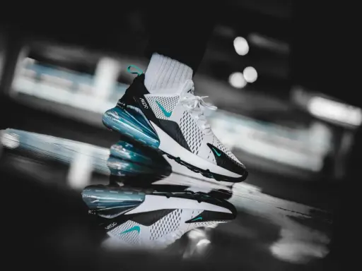 Ein stylischer Nike Air Max 270 in Weiß mit türkisen Akzenten, der auf einer spiegelnden Oberfläche steht. Ein zeitloser Klassiker unter den Nike Air Max alte Modelle.