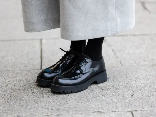 Schwarze Schnürschuhe mit dicker Sohle, ein moderner Schuh-Typ für Damen, kombiniert mit einem grauen Wollrock.