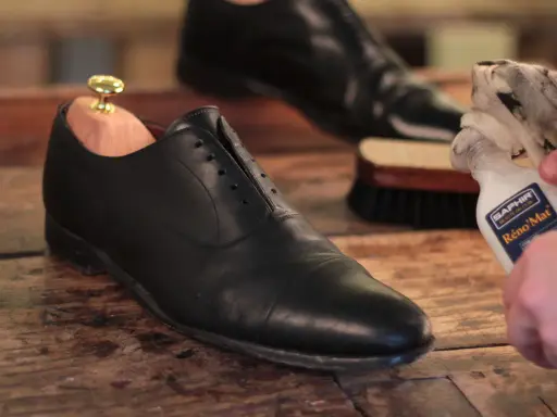 Schuhe polieren: Ein schwarzer Lederschuh mit Schuhspanner wird mit einem Tuch und Saphir Reno'Mat gereinigt.
