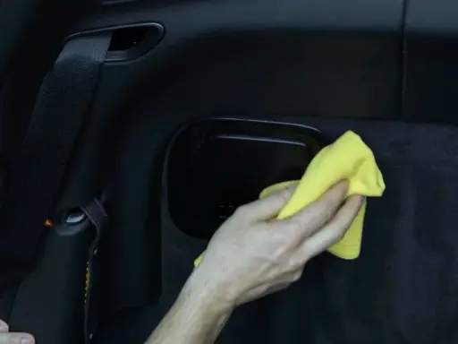 Hand wischt mit gelbem Tuch über schwarzes Kunstleder im Auto. So einfach ist Kunstleder reinigen.