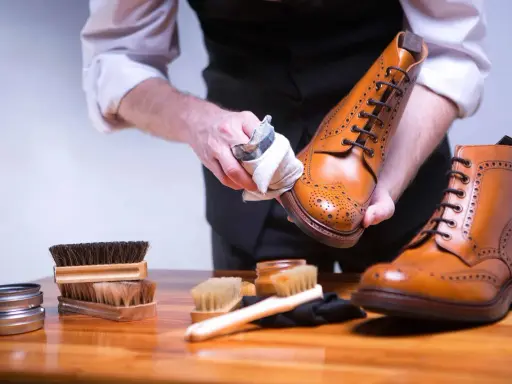 Mann poliert braune Glattleder-Schuhe mit einem Tuch. Pflege für Glattleder ist wichtig.