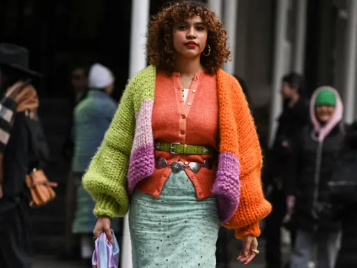 Bunte Strickjacke mit Ballonärmeln, die zeigt, wie man einen Cardigan kombinieren Damen kann. Dazu ein mintgrüner Rock und auffälliger Gürtel.