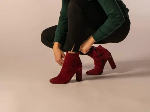 Eine Frau zieht rote Wildleder-Stiefeletten an. Verschiedene lederarten schuhe sind hier zu sehen, wie diese eleganten Damenschuhe.
