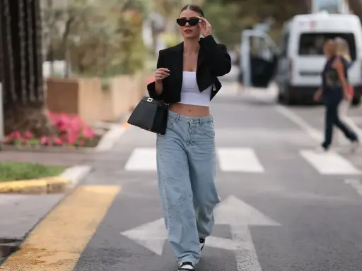 Frau in einem lässigen Baggy Jeans Outfit mit schwarzem Blazer und weißem Crop-Top, unterwegs in der Stadt.