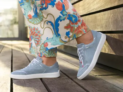 Blaue Wildlederschuhe mit weißer Sohle und dezenter Ziernaht am Schuh, kombiniert mit einer Hose mit floralem Muster.