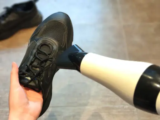 Schwarze Turnschuhe trocknen mit einem Föhn.