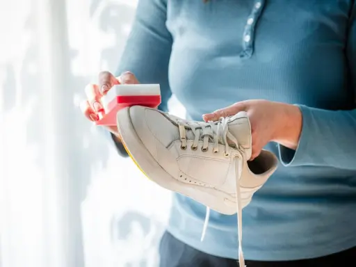 Person reinigt weiße Puma Schuhe mit einem Schwamm.