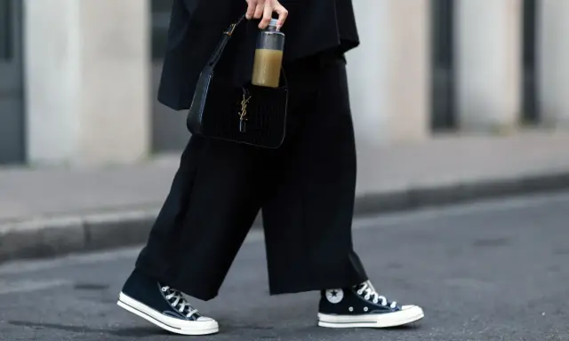 Schwarze, weite Hose und hohe Chucks kombinieren Damen für einen lässigen Look. Dazu eine schwarze Kroko-Tasche und eine Wasserflasche.