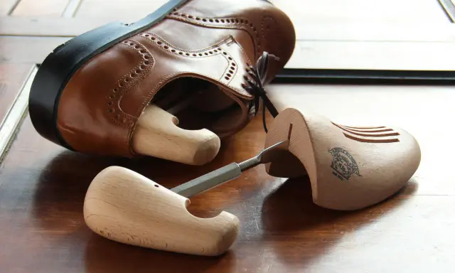 Holz-Schuhspanner für elegante Schuhe, die auch als Schuhspanner für Wanderschuhe dienen könnten, liegen neben einem braunen Lederschuh.