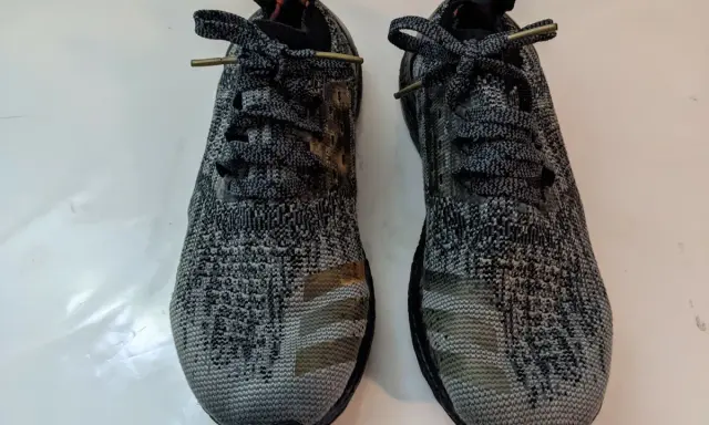 Zwei adidas bb3900 Laufschuhe mit grauem Camouflage-Muster und goldenen Streifen.