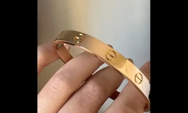 Vergleich: Fake Cartier Love Armband vs. echt. Ein glänzendes, roségoldenes Armband mit Schraubenmotiv wird von Fingern gehalten.