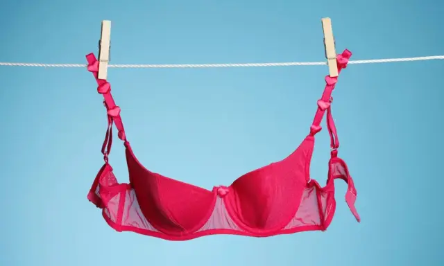 Ein roter BH mit Herzchen-Trägern trocknet an der Wäscheleine. Frisch gewaschen und bereit für den nächsten Einsatz.