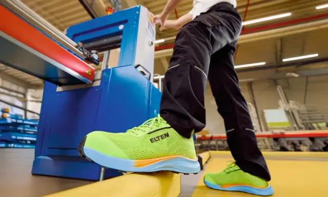 Arbeiter in leuchtend grünen Sicherheitsschuhen von ELTEN an einer Maschine. Seit wann gibt es Schuhe? Schon seit der Steinzeit, um die Füße zu schützen.