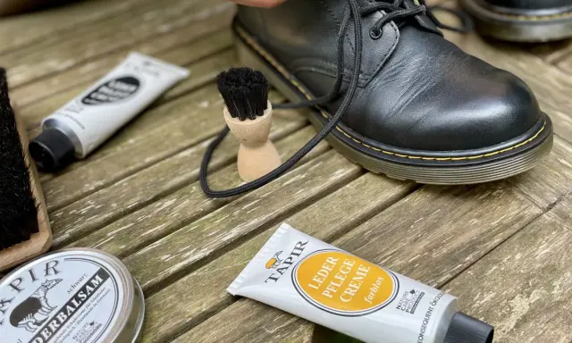 Schwarze Lederstiefel werden mit Tapir Lederpflegecreme und Bürsten gepflegt.